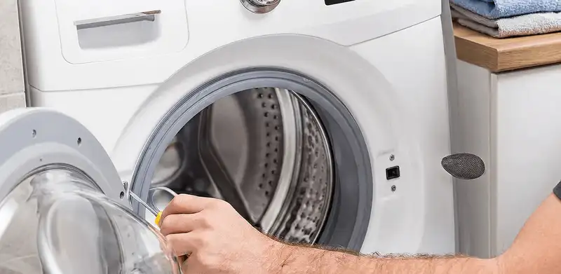 Handyman repairing a front-load washing machine and inspecting the drum in Fort Collins, CO